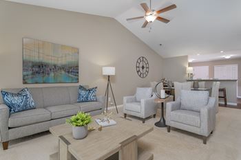 A living room with a grey couch, two chairs, a table, and a ceiling fan.